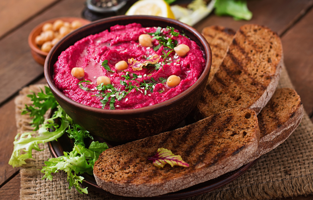 Roasted Beet Hummus with toast in a ceramic bowl on a wooden background