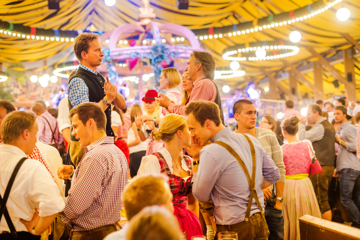 Munich, Germany - October 01, 2013: A group of young people, the women all dressed in dirndls, standing on the benches, dancing and having fun in the beer tent at the Octoberfest in Munich. The Oktoberfest is the largest fair in the world and is held annually in Munich.